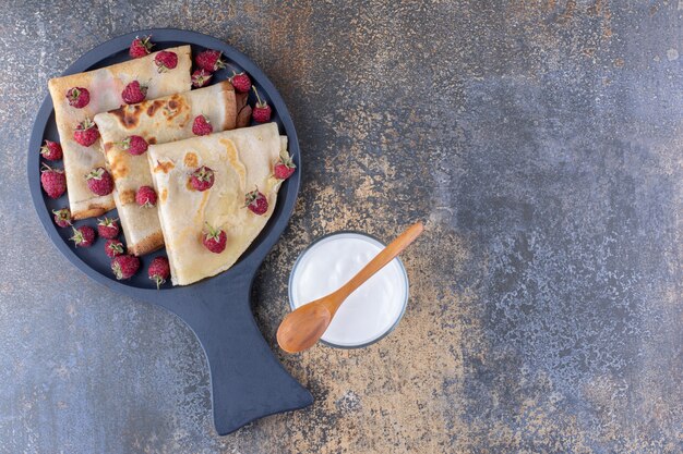 Crepes em uma travessa preta com framboesas e um copo de leite