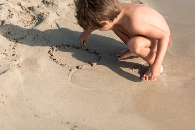 Foto grátis criança agachada brincando na areia