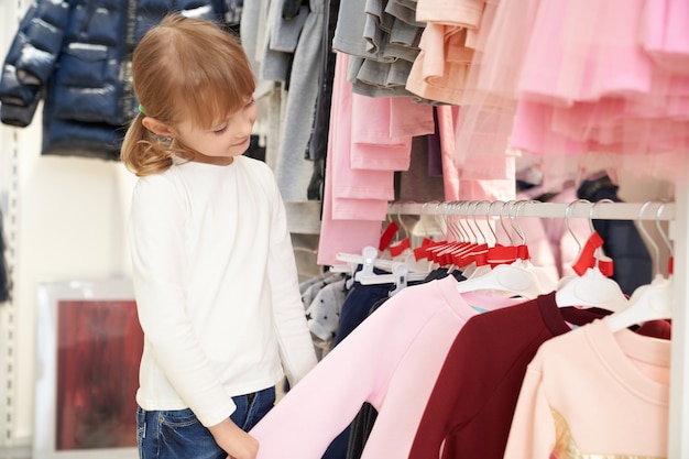 Criança bonita escolhendo roupas na loja.