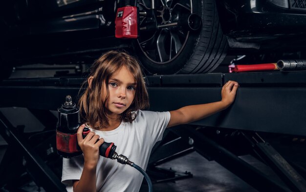 Criança bonitinha está posando para fotógrafo entregando broca pneumática na oficina do carro.