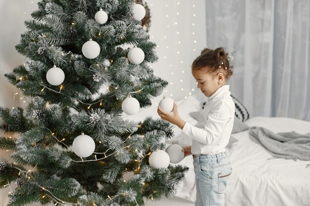 Criança com um suéter branco. Filha em pé perto da árvore de Natal.