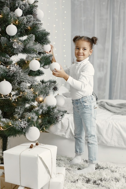 Criança com um suéter branco. filha em pé perto da árvore de natal.