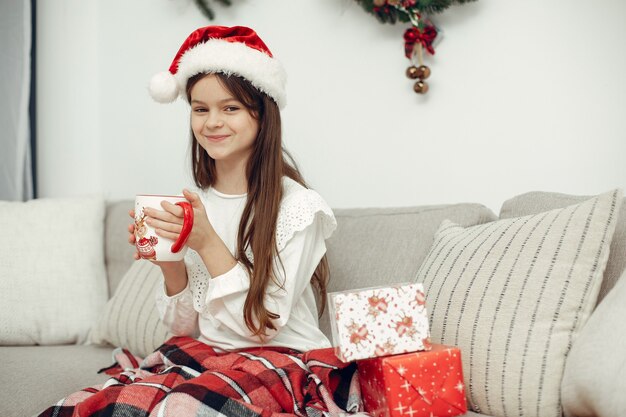 Criança com um suéter branco. Filha sentada perto da árvore de Natal.