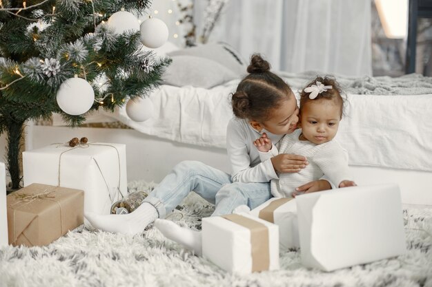 Criança com um suéter branco. Filhas stitting perto de árvore de Natal. Duas irmãs em casa.