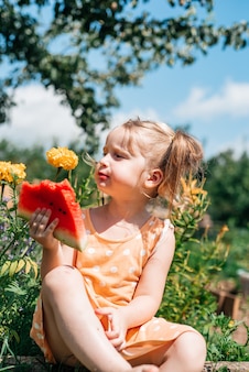Criança comendo melancia no jardim. as crianças comem frutas ao ar livre. lanche saudável
