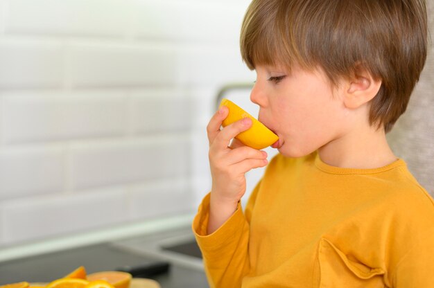 Criança comendo uma laranja na cozinha