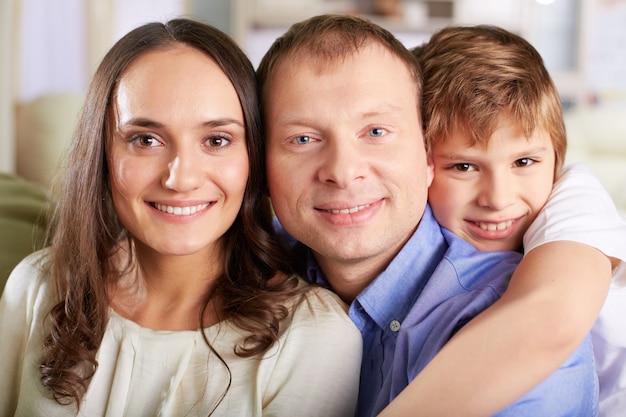 Criança de sorriso que abraça seus pais