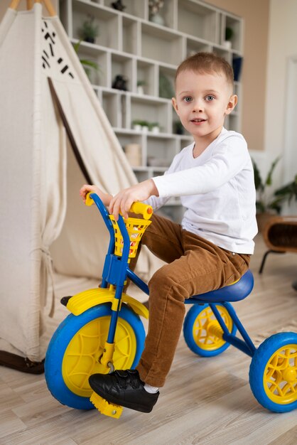 Criança de tiro completo andando de triciclo dentro de casa
