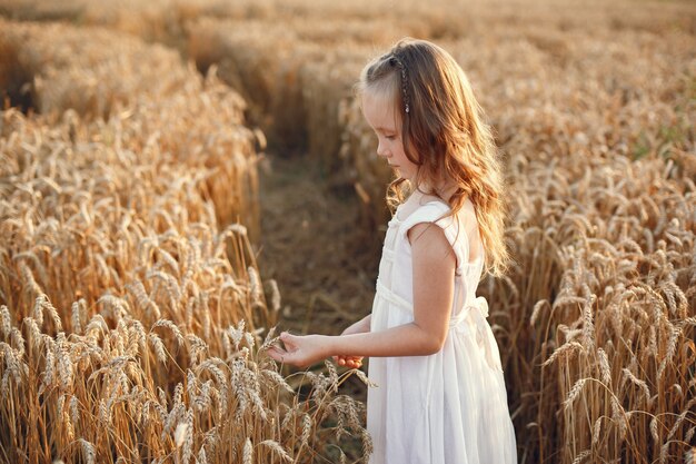 Criança em um campo de trigo de verão. Menina em um lindo vestido branco.