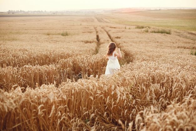 Criança em um campo de trigo de verão. Menina em um lindo vestido branco.