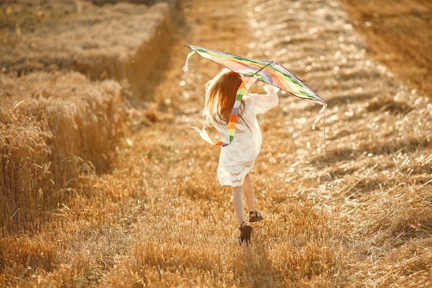 Criança em um campo de verão. Menina em um lindo vestido branco. Criança com uma pipa.