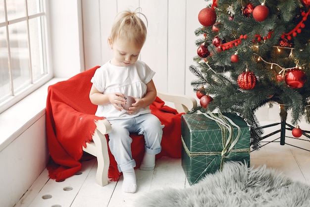 Criança em uma camiseta branca está jogando. Filha sentada perto da árvore de Natal.