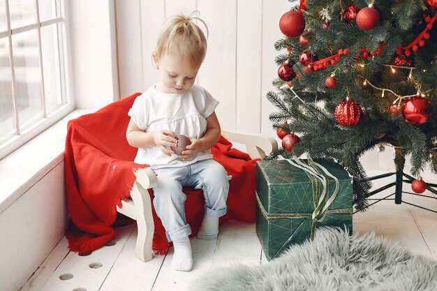 Criança em uma camiseta branca está jogando. Filha sentada perto da árvore de Natal.