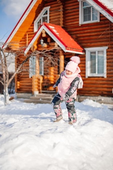 Criança está de pé na cabana de madeira, menina com terno quente de inverno, joga ao ar livre e gosta de su ...