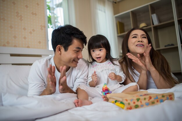 Criança feliz com os pais brincando na cama em casa