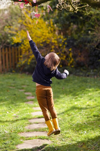 Criança loira fofa holandesa pulando em direção a um galho de árvore com flores no jardim
