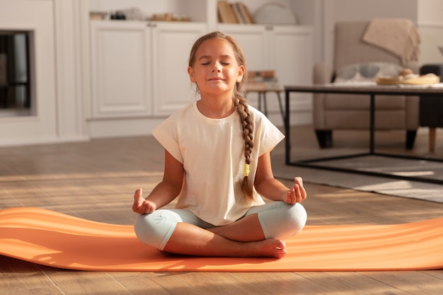 Criança meditando no tapete de ioga, tiro completo