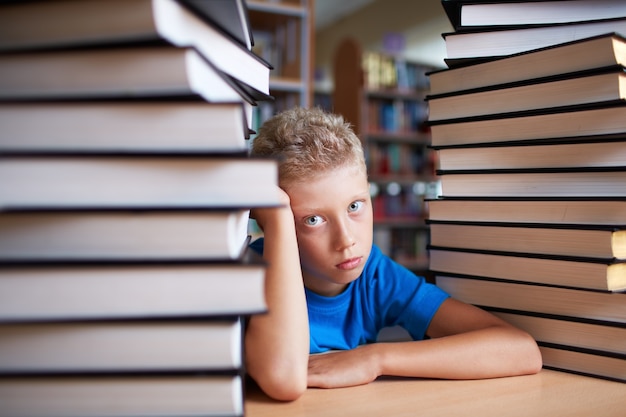 Criança pensativa cercado por livros pesados