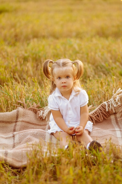 Criança pequena bonita em um vestido branco posando em campo verde e