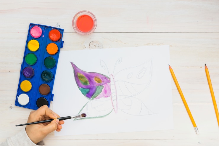 Foto grátis criança pequena pintando uma borboleta na página em branco com aquarela