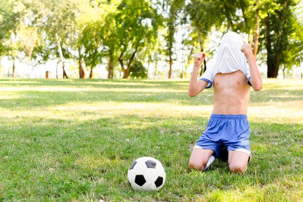 Criança sem camisa sendo vitoriosa após marcar um gol