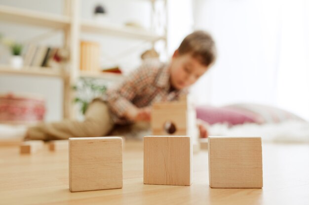 Criança sentada no chão, lindo menino brincando com cubos de madeira em casa