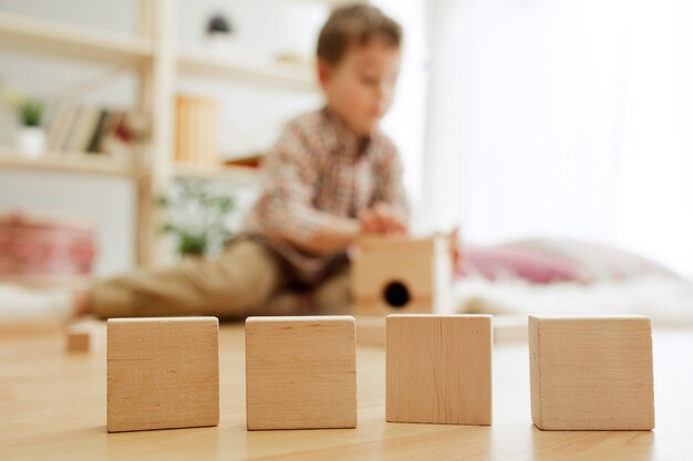 Criança sentada no chão. Menino bonito brincando com cubos de madeira em casa. Imagem conceitual com cópia ou espaço negativo