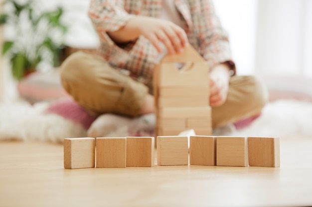 Criança sentada no chão. Menino bonito brincando com cubos de madeira em casa.