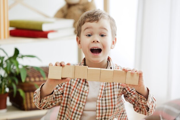 Criança sentada no chão. Menino muito sorridente surpreso brincando com cubos de madeira em casa. .