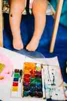 Foto grátis criança sentada perto de cores de água e papel