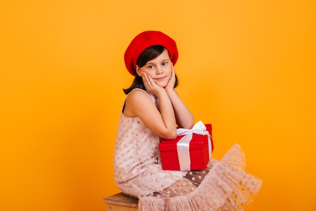 Criança sonhadora, posando com um presente de aniversário. garota pré-adolescente na boina vermelha, segurando o presente de ano novo.