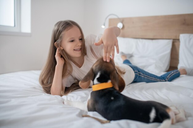 Criança sorridente do sexo feminino dando tapinhas na cabeça do beagle