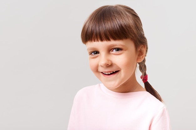 Criança sorridente encantadora usando um suéter rosa olhando para a frente com uma expressão feliz