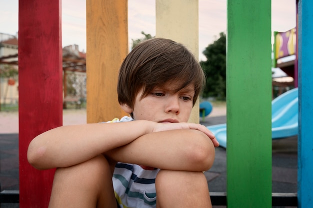Criança triste de tiro médio sentado ao ar livre