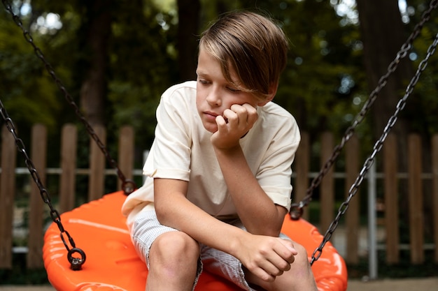 Foto grátis criança triste vista frontal sentado no balanço