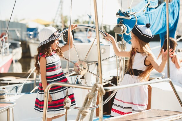 crianças a bordo do iate do mar bebendo suco de laranja. meninas adolescentes ou crianças contra o céu azul ao ar livre. Roupas coloridas. Conceitos de moda infantil, verão ensolarado, rio e feriados.