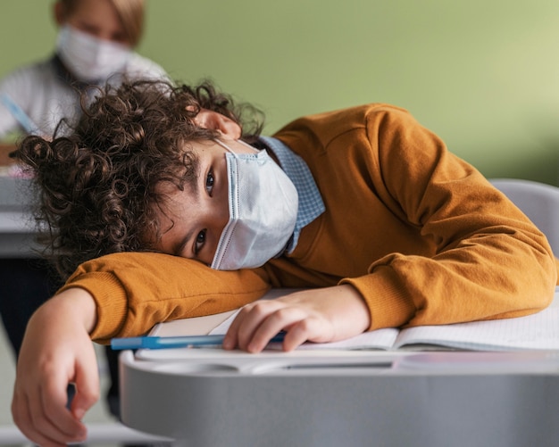 Crianças com máscaras médicas entediadas na aula na escola