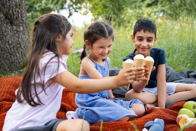 Foto grátis crianças comendo sorvete ao ar livre em um cobertor juntos