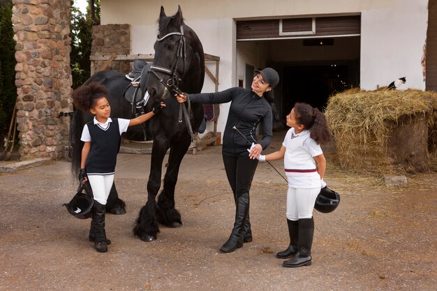 Crianças de tiro completo aprendendo a andar a cavalo