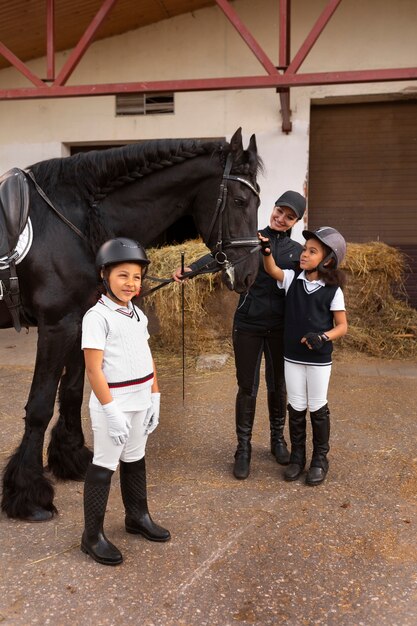 Crianças de tiro completo aprendendo a andar a cavalo