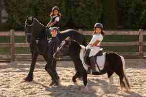 Foto grátis crianças de tiro completo aprendendo a andar a cavalo