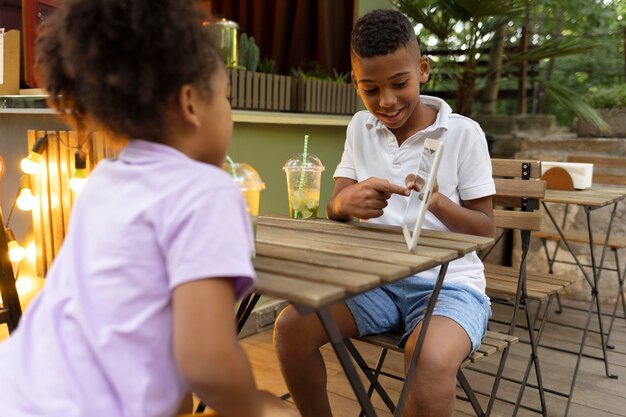 Crianças em filmagem média sentadas à mesa com um tablet