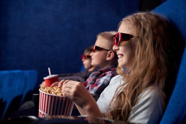 Crianças em óculos 3d sorrindo, assistindo filme no cinema.