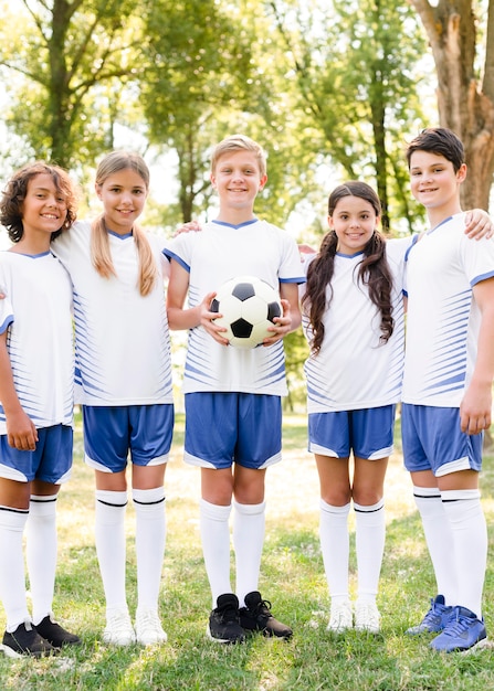 Crianças em roupas esportivas posando com uma bola de futebol