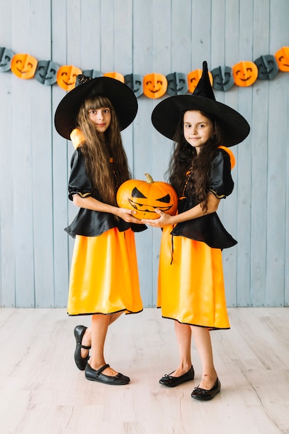 Crianças em trajes de bruxa segurando a abóbora de halloween