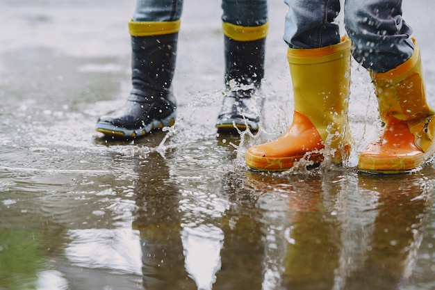 Crianças engraçadas em botas de chuva brincando com navio de papel por uma poça