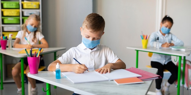 Crianças escrevendo na sala de aula usando máscaras médicas