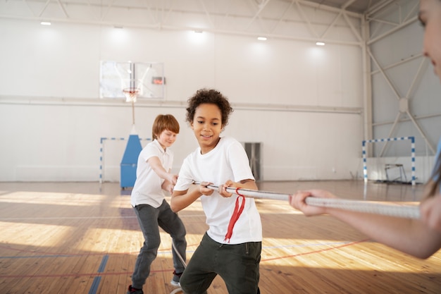 Crianças esportivas fortes puxando corda no ginásio