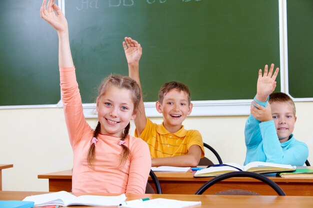 Crianças felizes com os braços para cima sentado na sala de aula