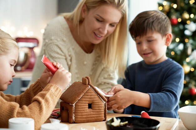 Crianças felizes decorando uma casa de pão de gengibre com a mãe